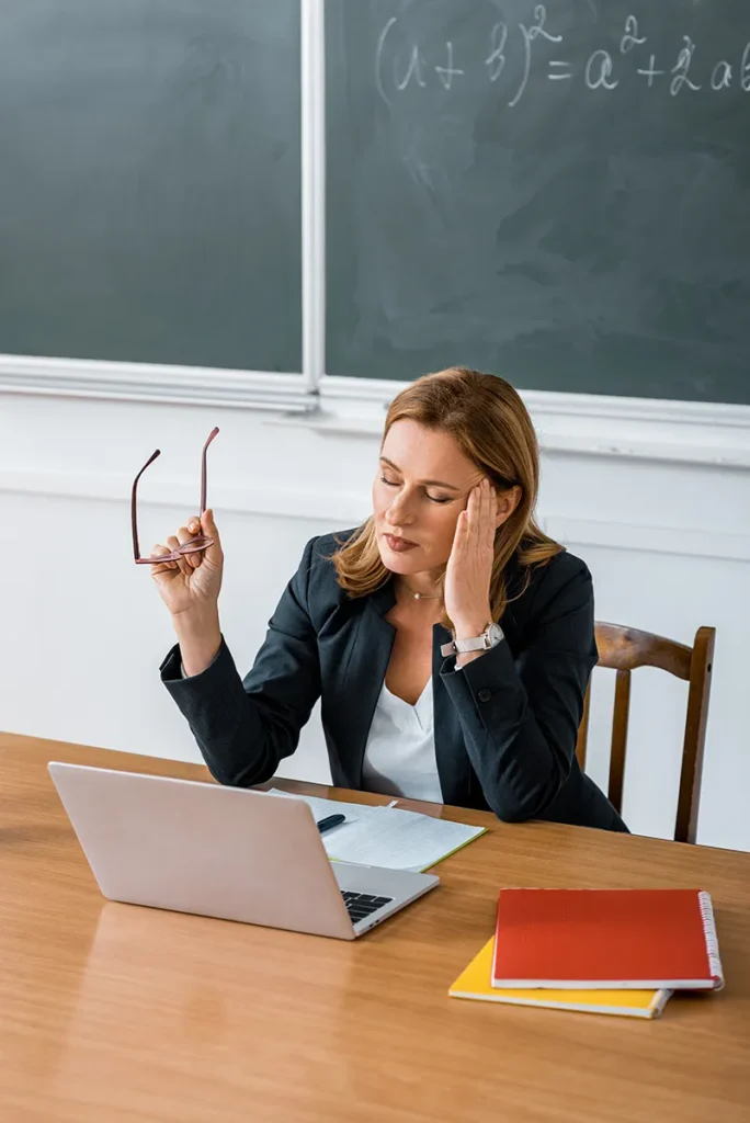 Gestresste Lehrerin mit Brille in der Hand – Stress im Lehrberuf, Online-Unterstützung für Lehrkräfte
